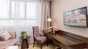 A hotel room with a sofa, armchair, small table with a vase of flowers, a desk with a lamp, and a TV on the wall. - Shanghai Pudong Airport Yueshangju Hotel (Shanghai)