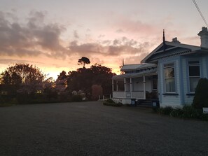 A two-story house with a porch and a garage, surrounded by trees and a gravel driveway. - Lancewood Lodge (Bulls)