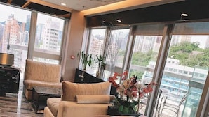 Um lobby de hotel moderno com um sofá, cadeiras, uma mesa redonda e grandes janelas com vista para a cidade.