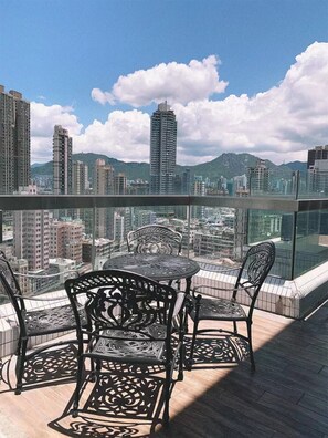 Un balcón con mesa y sillas, que ofrece vista a la ciudad, con edificios altos y montañas al fondo.
