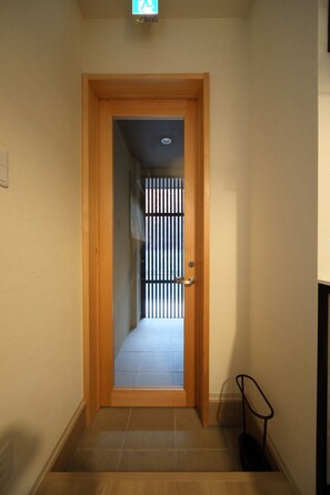 Um corredor estreito com uma porta de madeira que dá para um quarto com chão de azulejos.