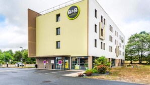A B&B hotel with a modern design, featuring a prominent logo, a ground-level entrance, and a parking area. - B&B Hotel Nantes Savenay (Savenay)