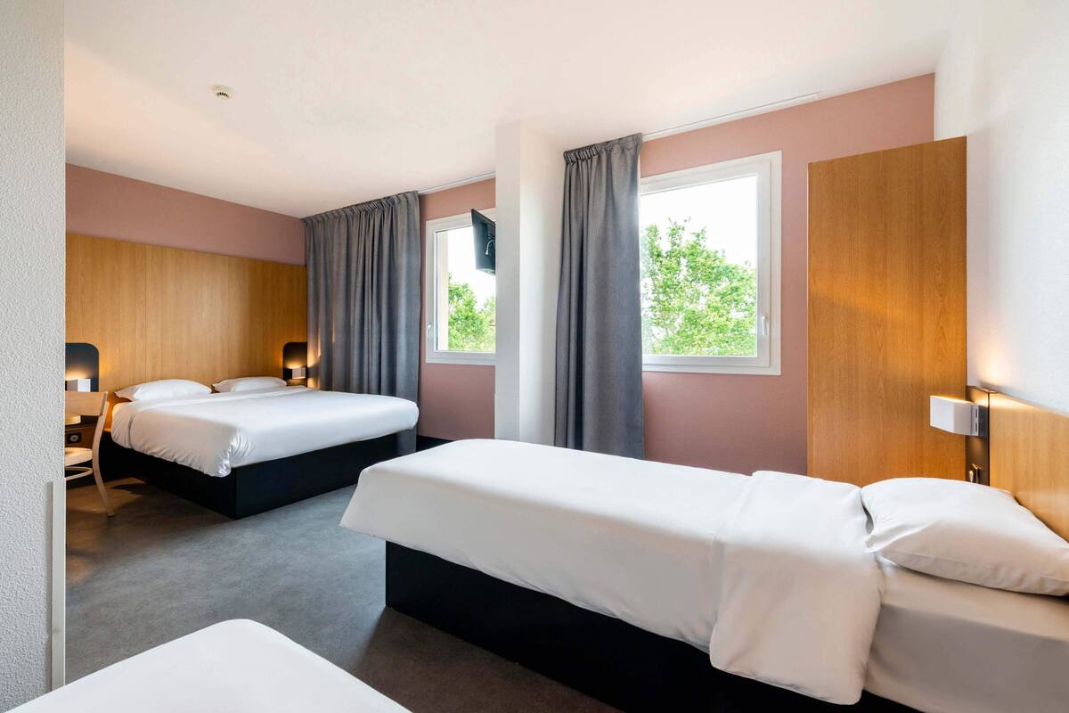 Hotellihuone, jossa on kaksi sänkyä, työpöytä ja ikkuna, jossa on verhot.