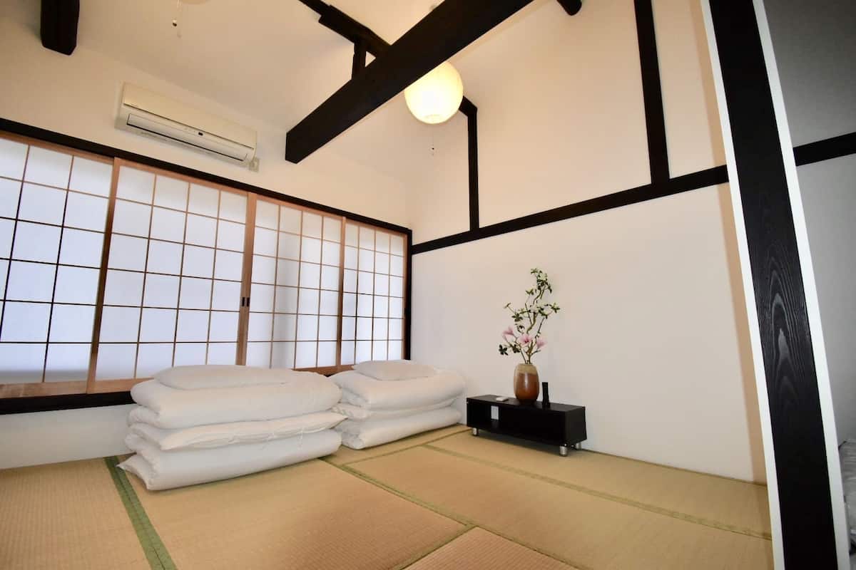 A traditional Japanese room with tatami flooring, a shoji screen, and a small table with a vase of flowers.