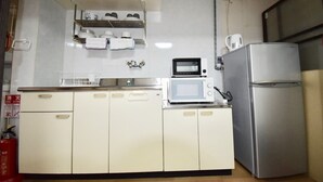 A compact kitchen with white cabinets, a microwave, a refrigerator, and a shelf with dishes and a kettle. - Kumoi Jurakumawari (Kyoto)