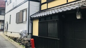 A multi-story building with a traditional facade, featuring a yellow and white color scheme, a black gate, and a tiled roof. - Kumoi Jurakumawari (Kyoto)