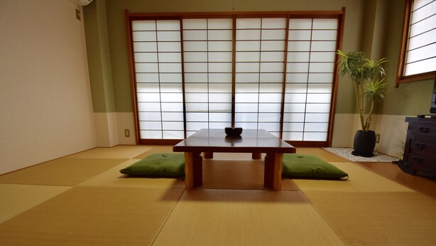 A tatami mat room with a low wooden table, two green cushions, a potted plant, and a sliding shoji screen. - Kumoi Tofukuji (Kyoto)