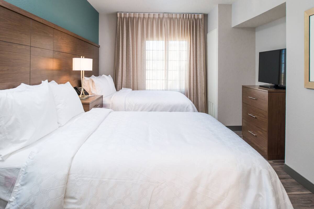 Une chambre d’hôtel avec deux lits, une télévision, une commode et une fenêtre avec des rideaux.