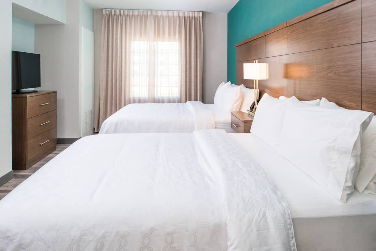 Une chambre d’hôtel avec deux lits, une télévision, une commode et une fenêtre avec des rideaux.