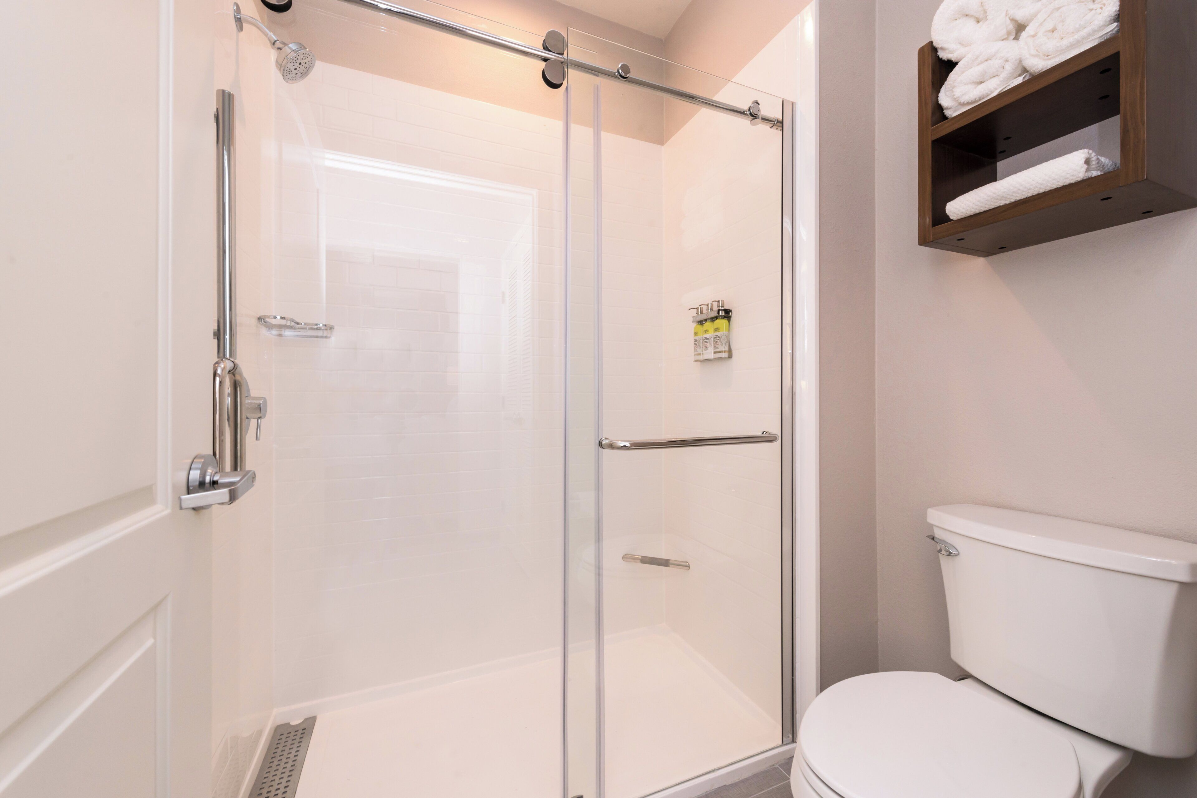 A bathroom with a glass-enclosed shower, a white toilet, and a shelf with towels.