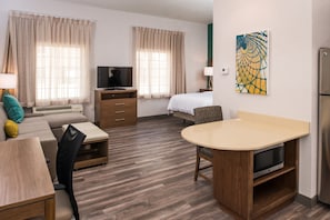 A hotel room with a bed, a TV, a desk with a microwave, a sofa, and a dining table. - Staybridge Suites Pecos by IHG (Pecos)