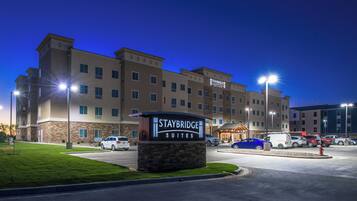 Un hotel Staybridge Suites con un letrero, estacionamiento y varios vehículos.