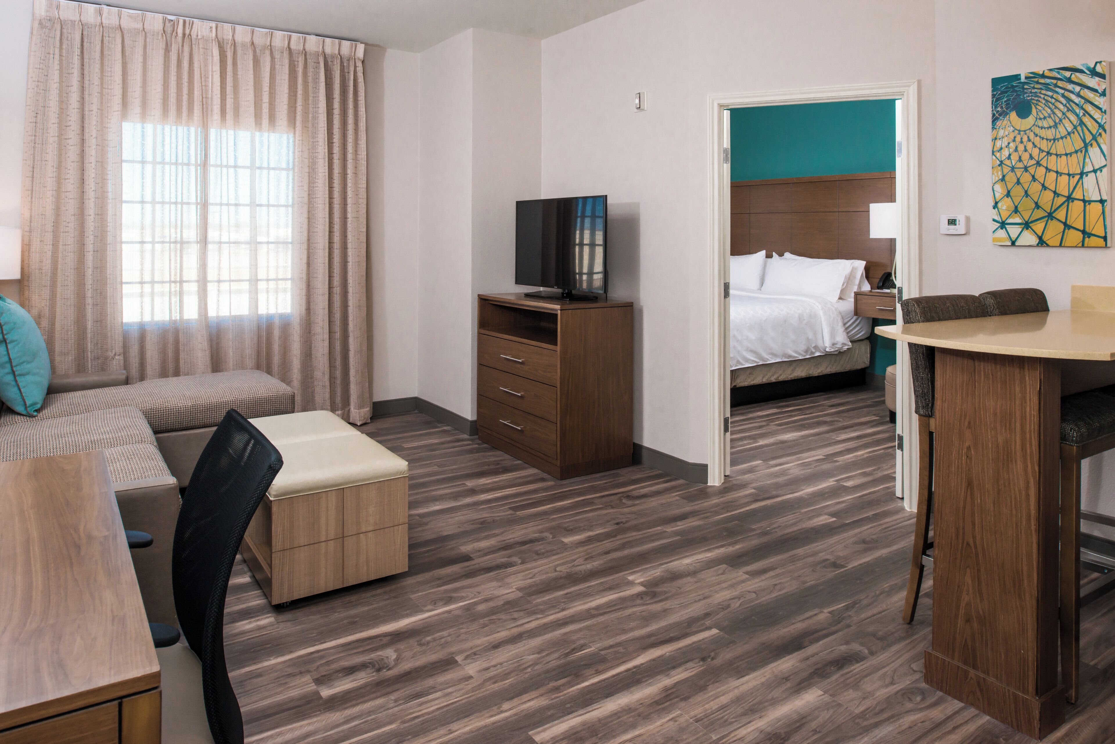 A hotel room with a bed, a desk, a chair, a TV, and a bathroom visible through an open door.