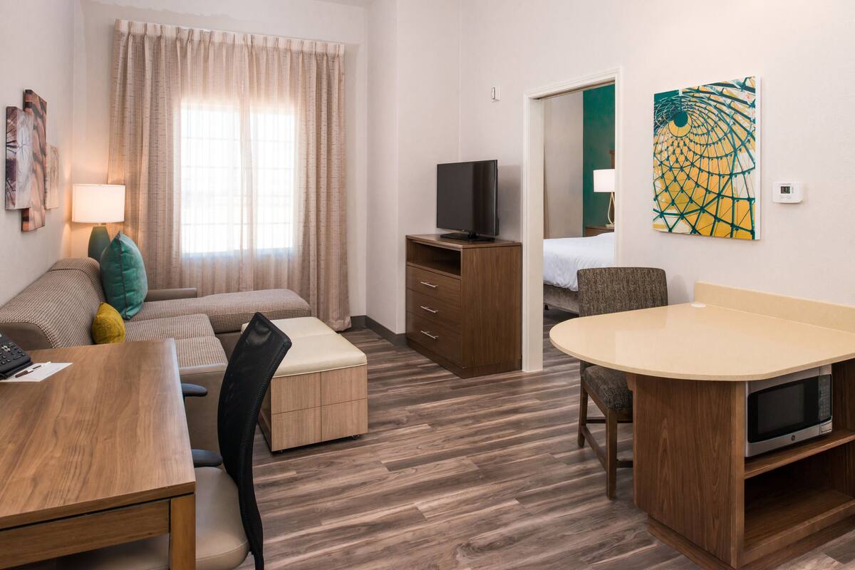 Une chambre d’hôtel avec un canapé, une petite table en bois, un téléviseur posé sur un meuble, un four à micro-ondes et un tableau accroché au mur.