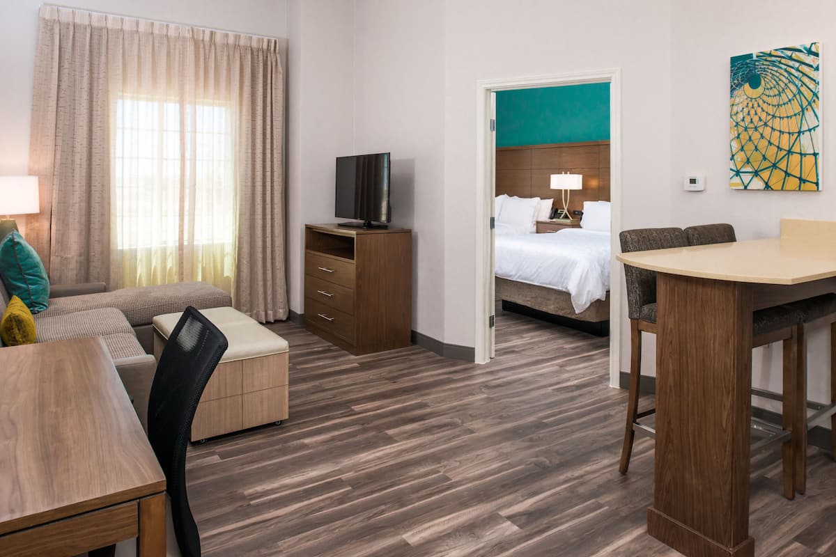 Une chambre d’hôtel avec un plancher en bois, un canapé, une table à manger, une télévision, un lit et un tableau au mur.