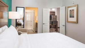 A hotel room with a bed, a sitting area with a chair and a table, a bathroom, and a kitchenette.