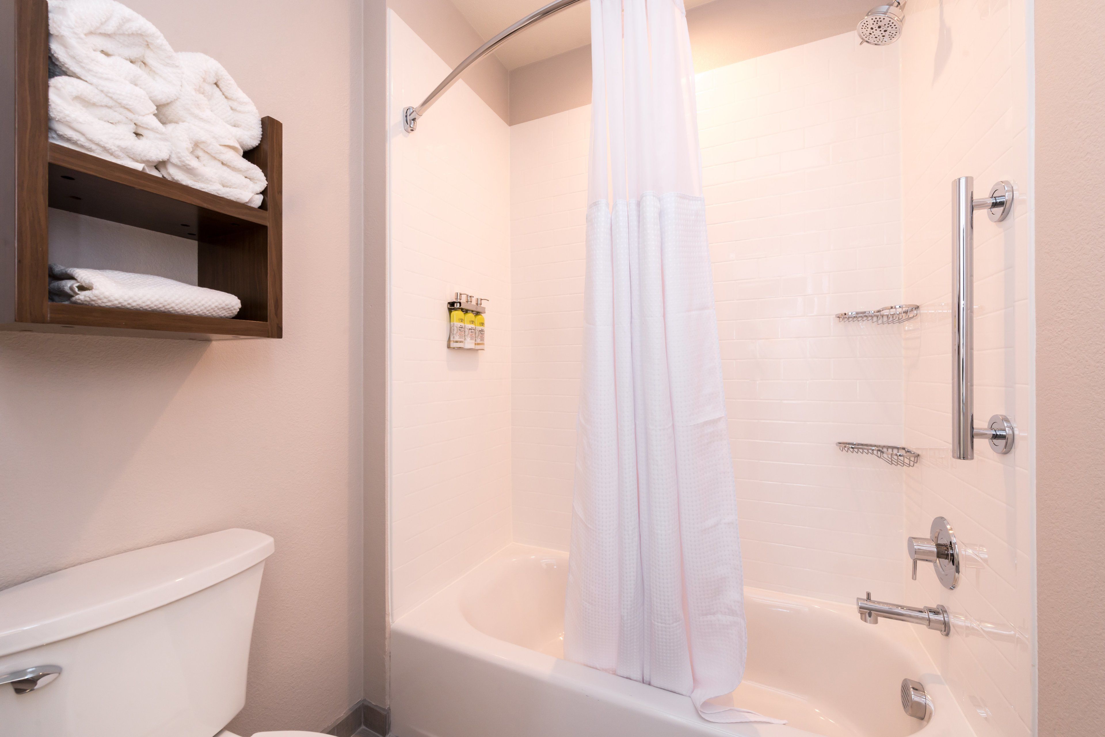 A bathroom with a bathtub, a toilet, and a shelf with folded towels.