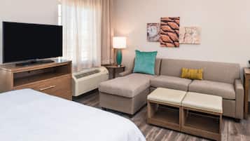 A modern hotel room with a flat-screen TV, a sofa, a bench, a desk, and a lamp.