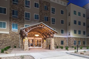 A hotel entrance with a stone facade, multiple windows, and a covered entrance area with a bench. - Staybridge Suites Pecos by IHG (Pecos)