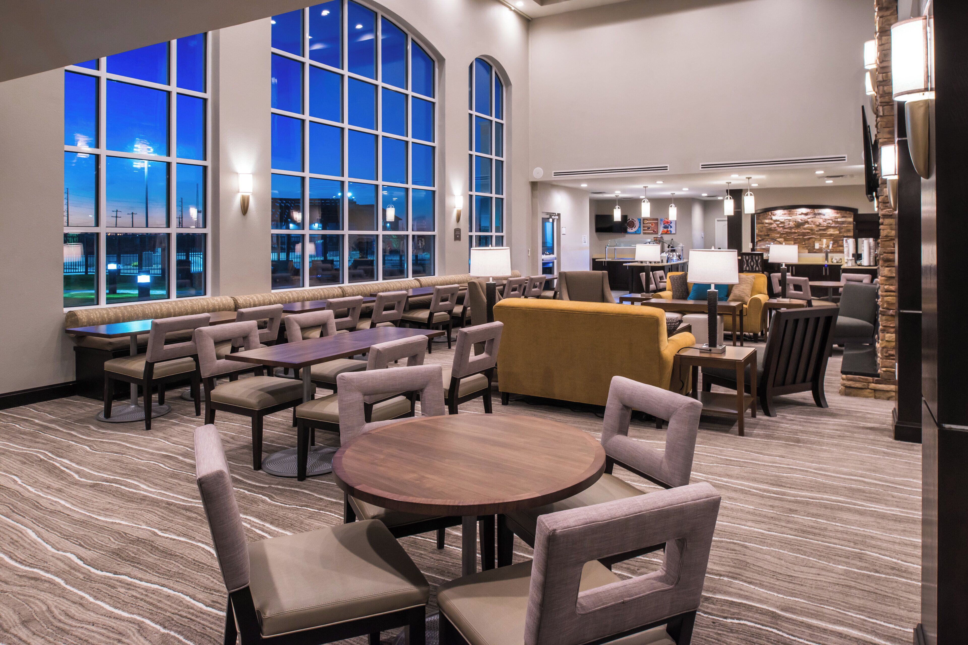 A hotel lobby with a seating area, a bar, and a kitchen in the background.