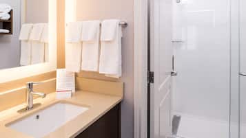 Une salle de bain équipée d’un lavabo, d’un miroir, d’un porte-serviettes et d’une porte de douche en verre.