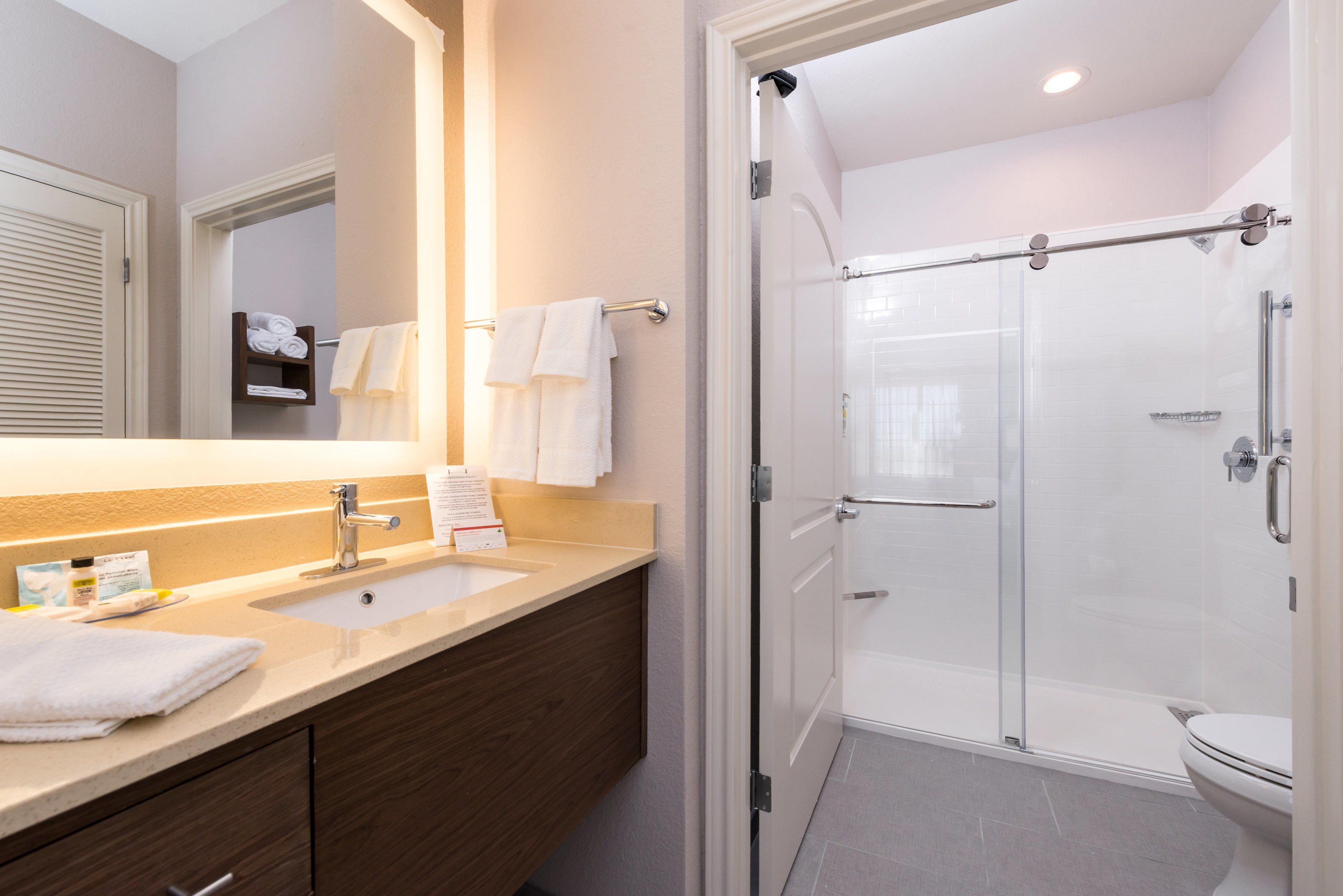 A modern bathroom with a large mirror, two sinks, a glass shower enclosure, and a toilet.