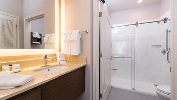 A modern bathroom with a large mirror, two sinks, a glass shower enclosure, and a toilet.