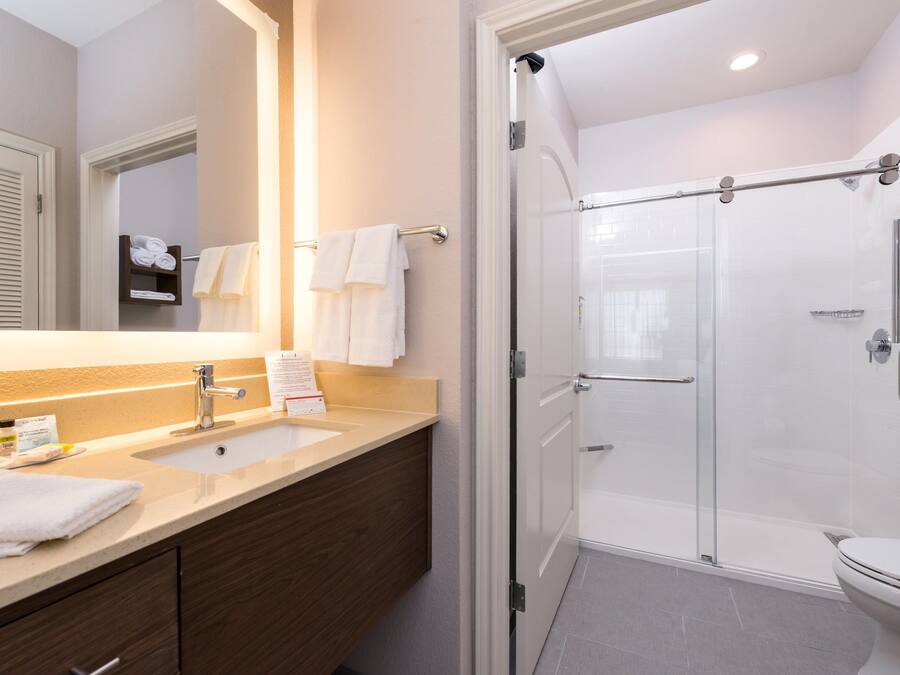 A modern bathroom with a large mirror, two sinks, a glass shower enclosure, and a toilet.