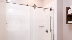 A glass-enclosed shower with a metal grab bar, a towel rack, and a wall-mounted towel dispenser.