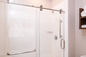 Une douche fermée par des parois en verre, dotée d’une barre d’appui en métal, d’un porte-serviettes et d’un distributeur de serviettes fixé au mur.