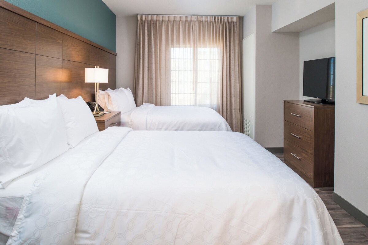 Une chambre d’hôtel avec deux lits, une télévision, une commode et une fenêtre avec des rideaux.