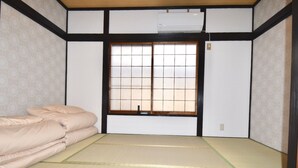 Una habitación japonesa tradicional con suelo de tatami, futón, puertas correderas shoji y aire acondicionado instalado en el techo.
