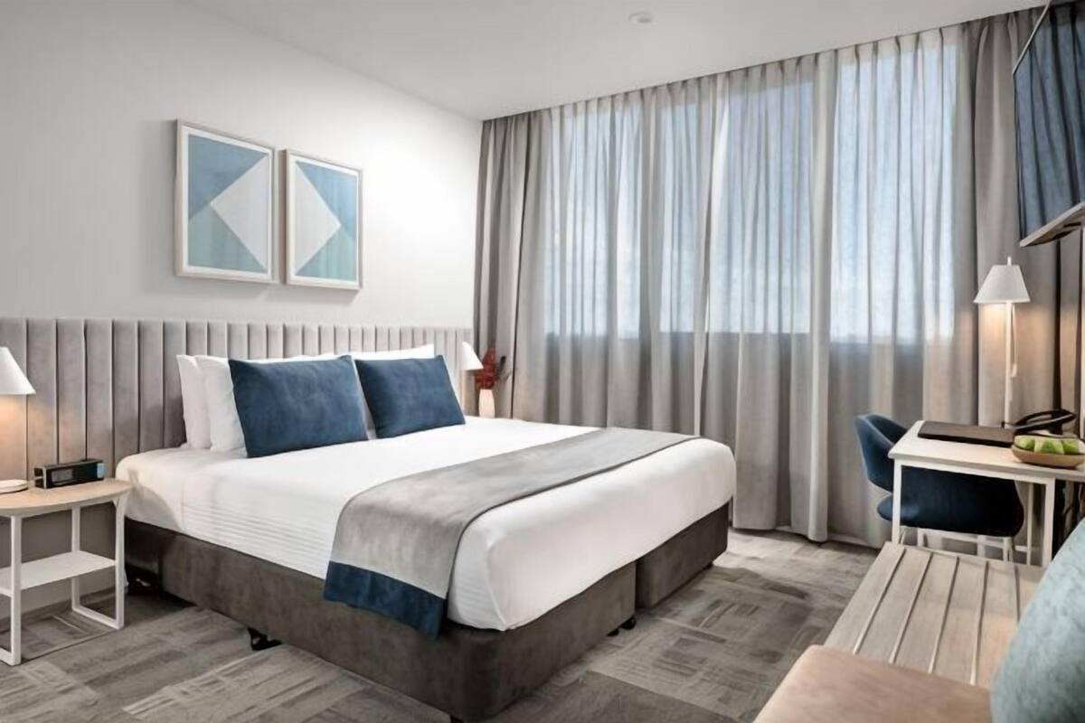 A modern hotel room with a large bed, a desk, and a chair.