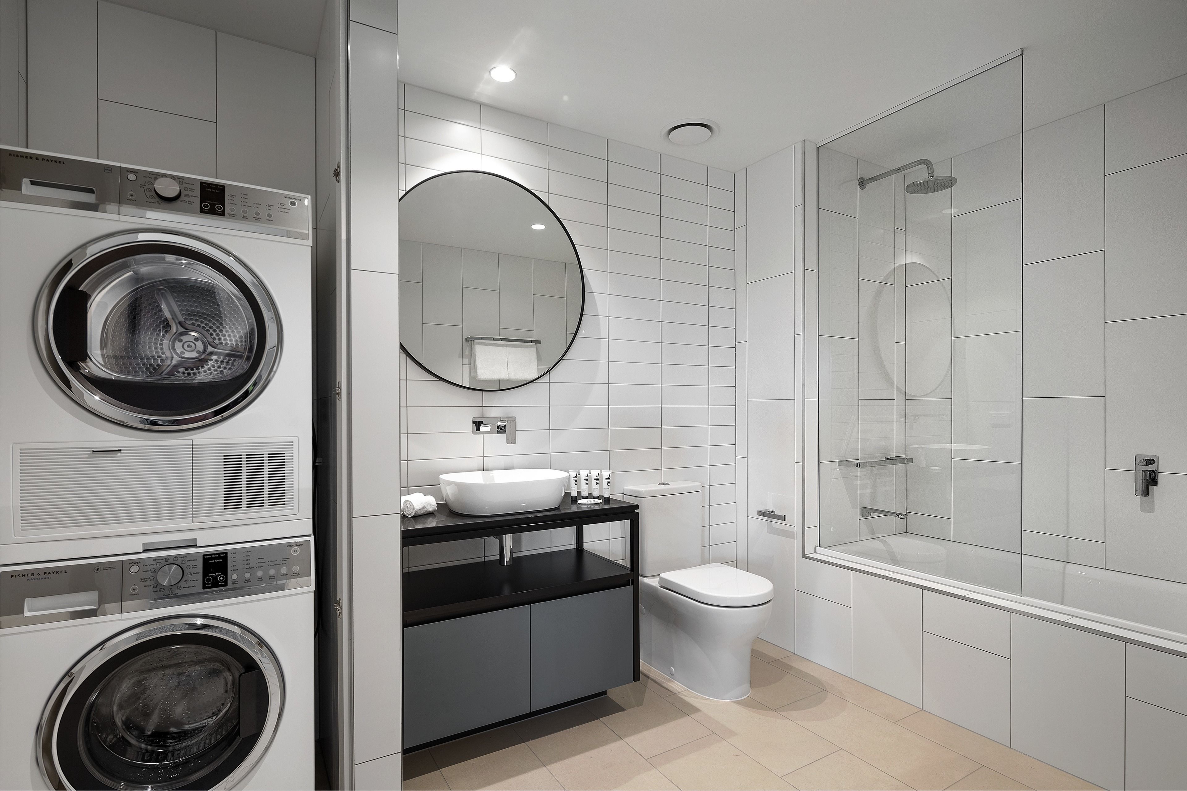 Un baño moderno con lavadora incorporada, lavamanos, inodoro y ducha con mampara de vidrio.