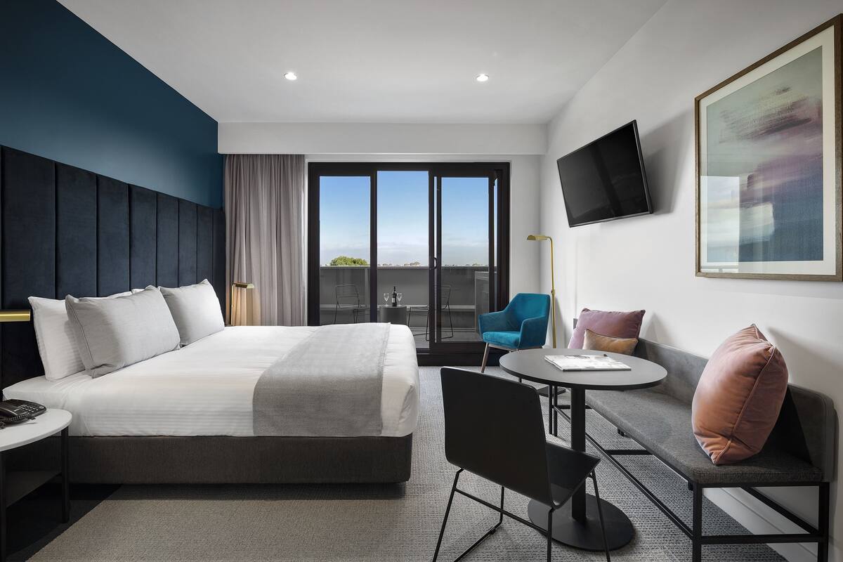 A modern hotel room with a large bed, a sofa, a small table, and a TV mounted on the wall.