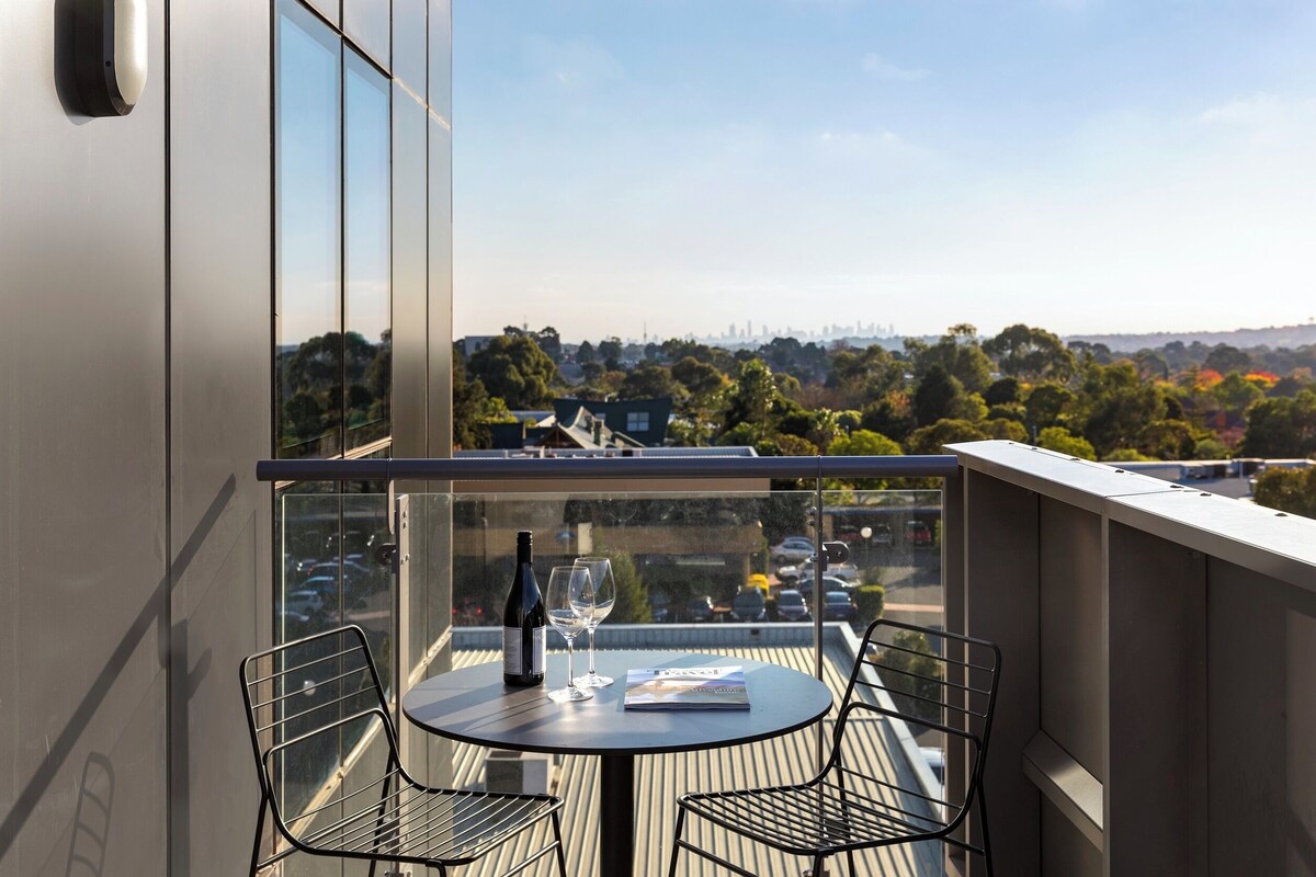 A balcony with a table, chairs, a bottle of wine, and a magazine.