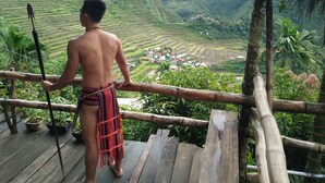 A person standing on a wooden deck overlooking terraced fields and a small village. - Batad View Inn and Restaurant (Banaue)