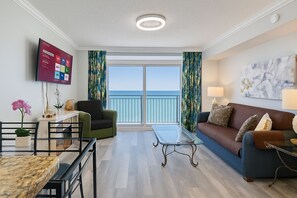 Un salon moderne avec balcon, un téléviseur à écran plat, un coin repas et un canapé agrémenté de coussins.