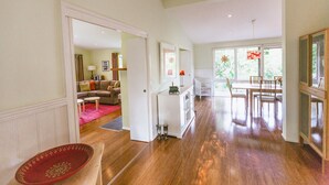 A spacious living area with a wooden floor, a dining table with chairs, a white sofa, and a red decorative bowl. - Riverdale - An escape from the Yarra Valley (Wesburn)