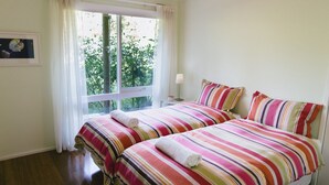 A room with two beds, a window with curtains, a bedside table with a lamp, and a framed picture on the wall. - Riverdale - An escape from the Yarra Valley (Wesburn)