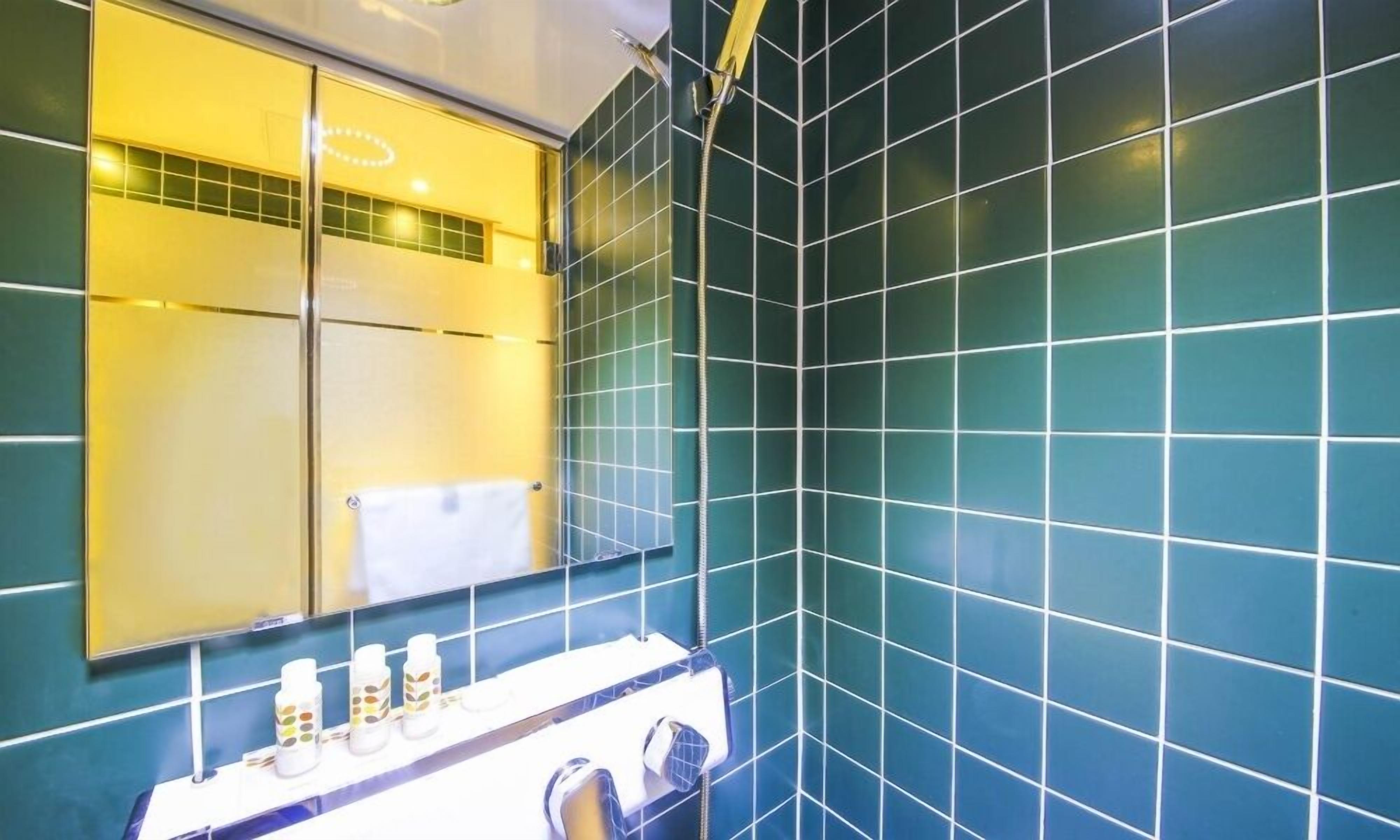 A bathroom with teal tiles, a mirror, a towel rack, and a sink with toiletries.