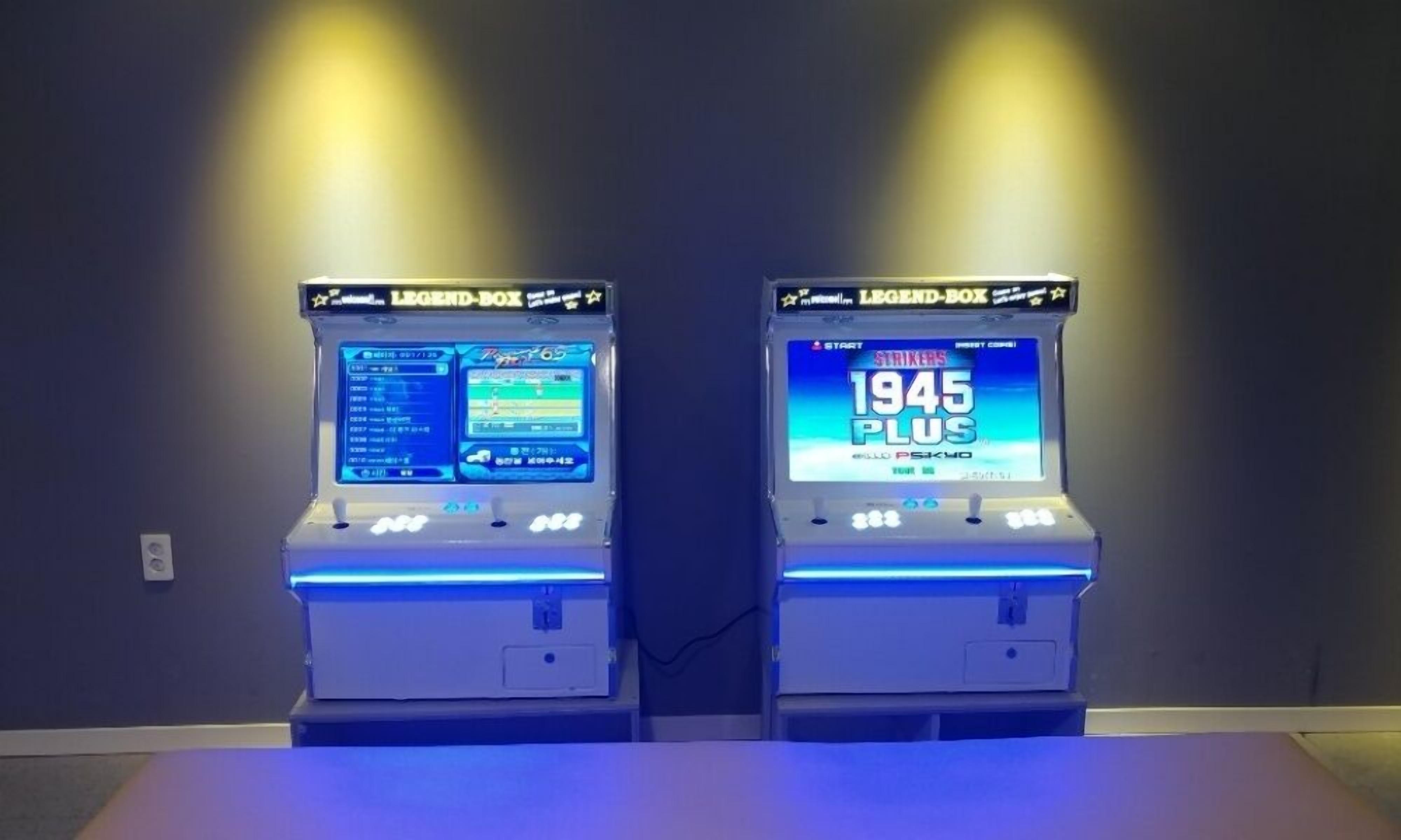 Dos máquinas de arcade con la etiqueta 'LEGEND-BOX' y una pantalla digital, situadas frente a una pared oscura.