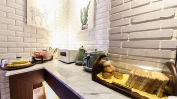 A kitchen with white brick walls, a marble countertop, a bread display case, and a coffee machine.
