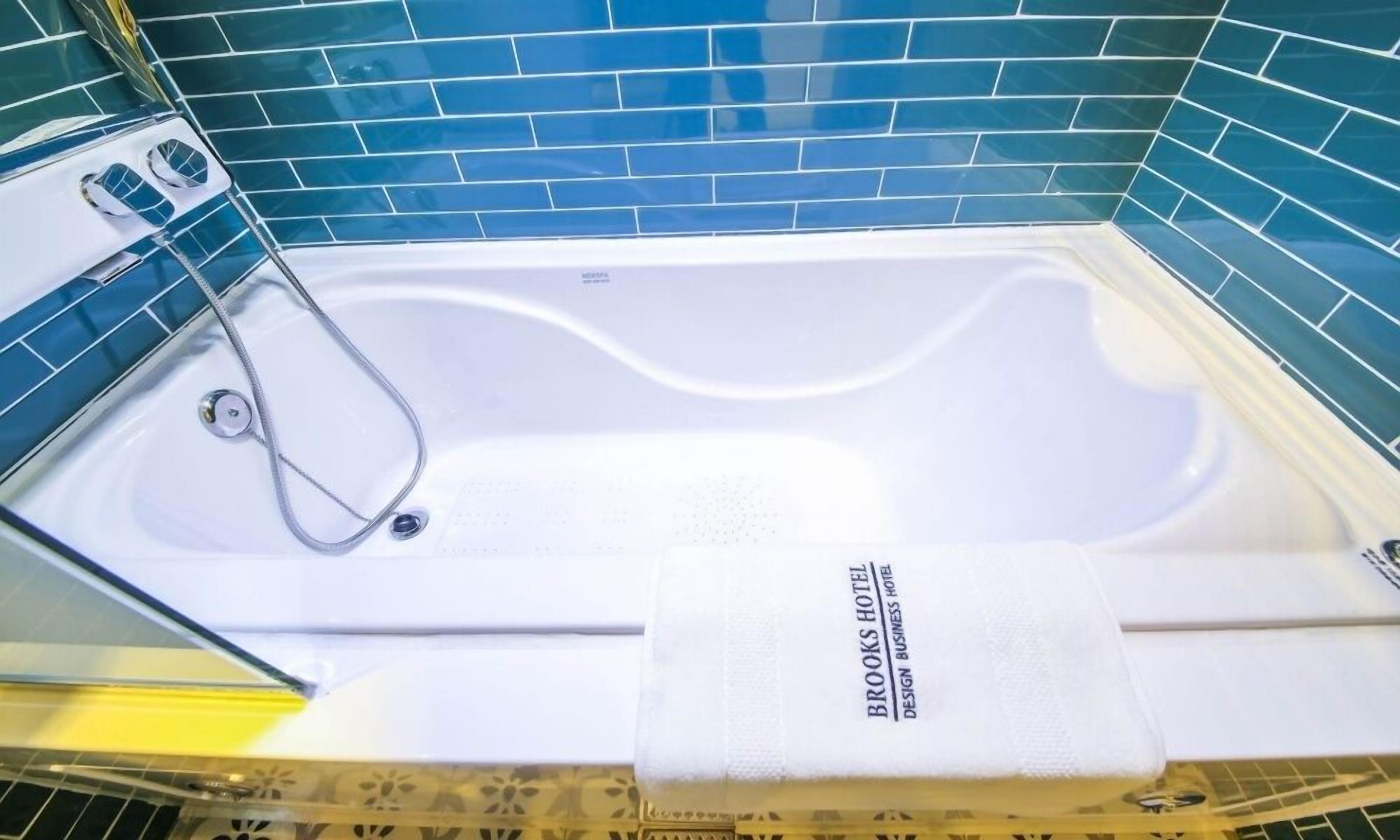 Une baignoire blanche avec une pomme de douche, une serviette et une pancarte sur laquelle on peut lire : « BROOKS HOTEL, HÔTEL D’AFFAIRES AU DESIGN UNIQUE ».
