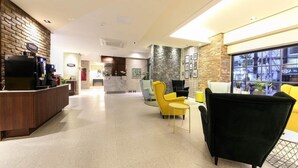 Un hall d’hôtel comprenant un comptoir d’accueil, un espace salon avec des fauteuils, une machine à café et une grande fenêtre.