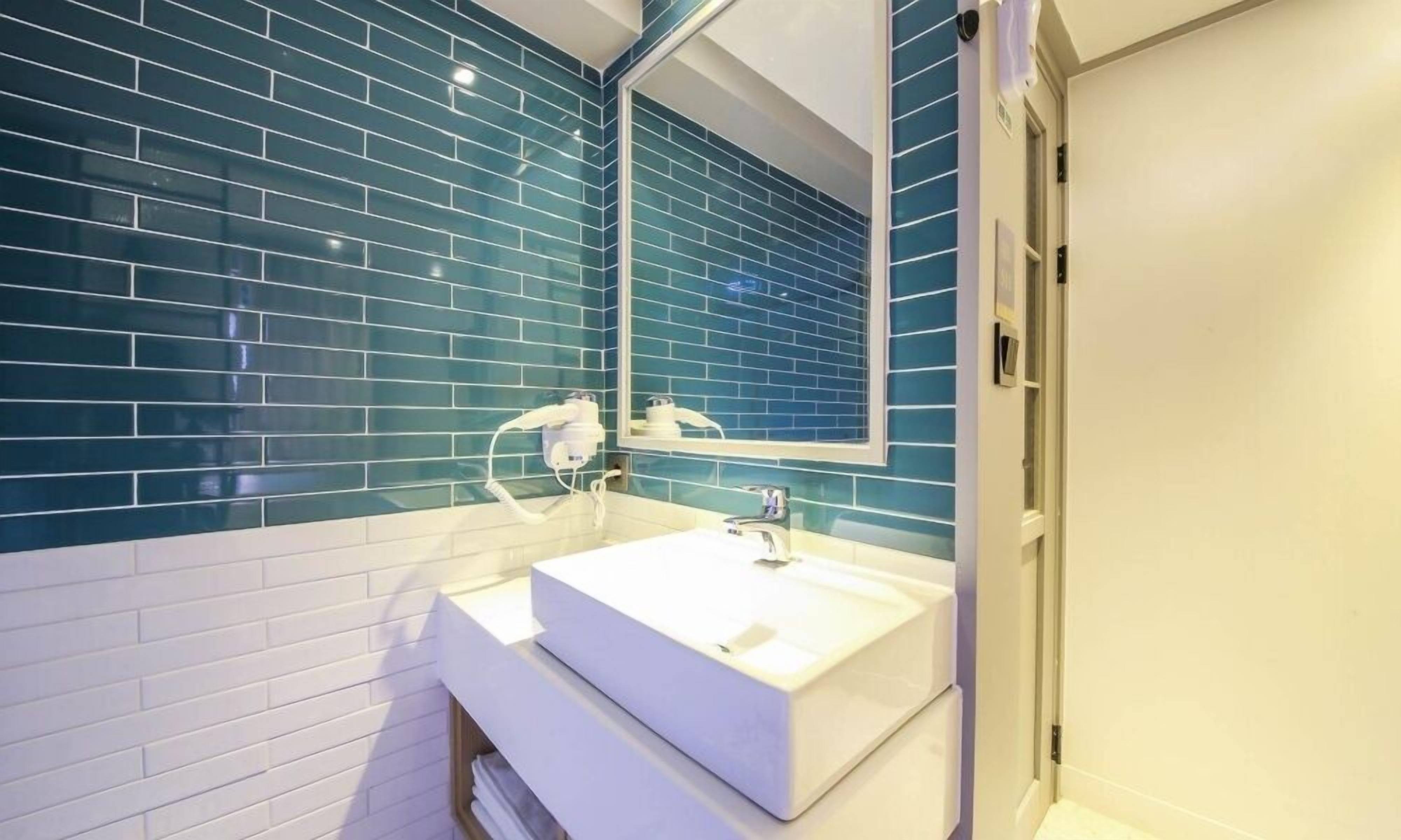 Een badkamer met een wit wastafelmeubel, een spiegel en blauwe betegelde wanden.