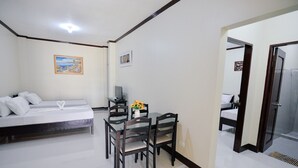 Habitación de hotel con cama, una pequeña mesa de comedor con sillas, televisión y baño a la vista a través de una puerta abierta.