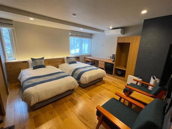 Ein Zimmer mit zwei Betten, einem Schreibtisch, einem Stuhl und einer kleinen Küchenzeile.