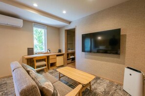 A living room with a sofa, a coffee table, a TV mounted on the wall, and a desk with a chair.