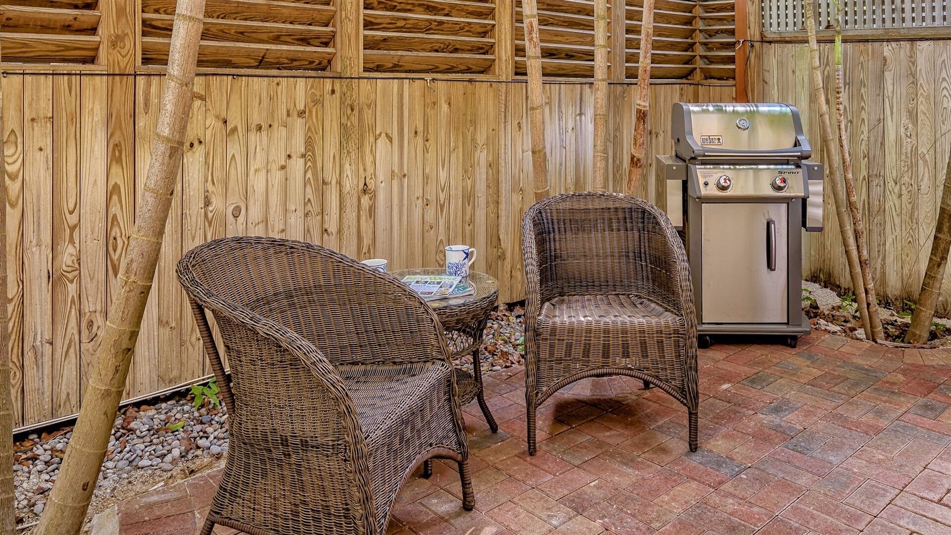 En terrasse med fletstole, et lille bord og en grill.